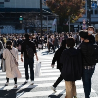 A family walks across the Shibuya scrambling crossing in Tokyo on Sunday alongside throngs of pedestrians. | RYUSEI TAKAHASHI
