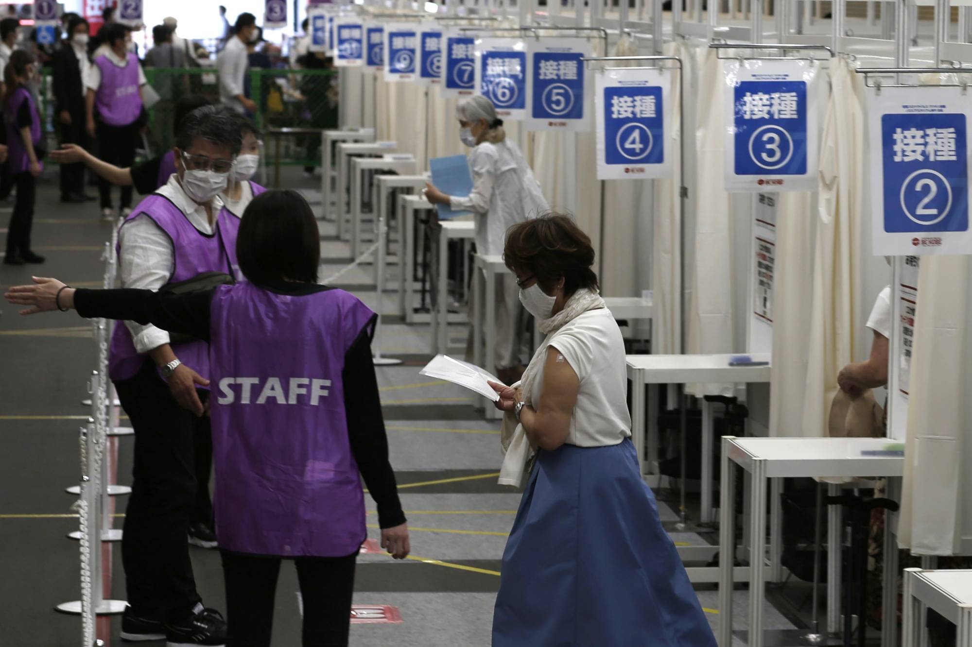A woman walks away from vaccination booths after receiving a dose of the Pfizer-BioNTech COVID-19 vaccine at a mass inoculation site at Noevir Stadium Kobe in June. | BLOOMBERG