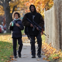 Erick Jordan carries a rifle while explaining gun safety to his 9-year-old son, Daemeon after the verdict in the trial of Kyle Rittenhouse, in Kenosha, Wisconsin, on Friday. | REUTERS