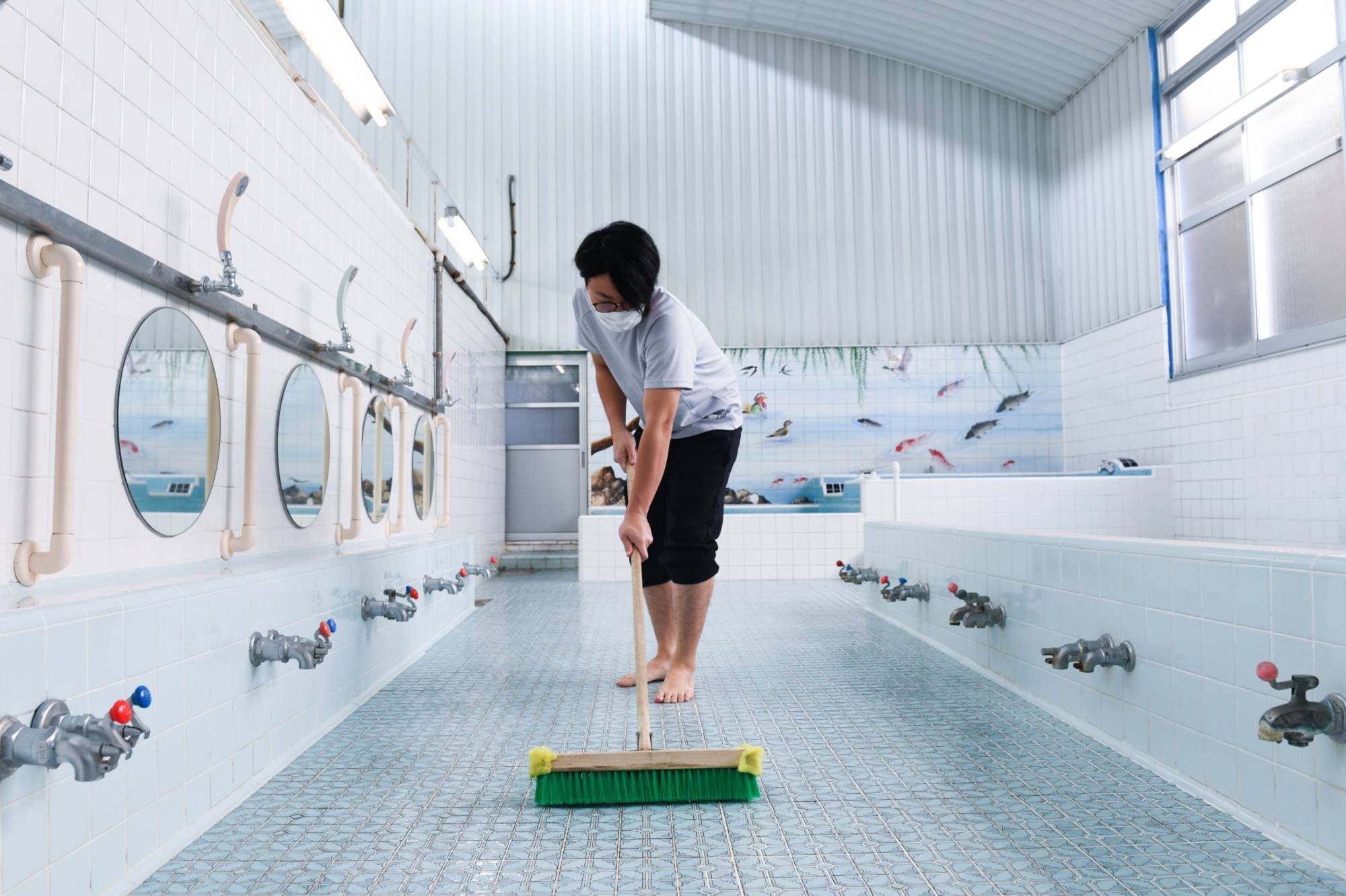 Atsushi Tsukui cleans the floor before opening the Uenoyu bathhouse in Kiryu, Gunma Prefecture, on Saturday. | BLOOMBERG