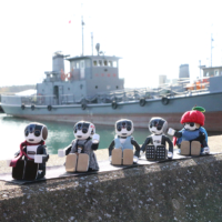 RoBoHoN robots arrayed with the Ominato base of the Maritime Self-Defense Force in the background. | MUTSU CITY