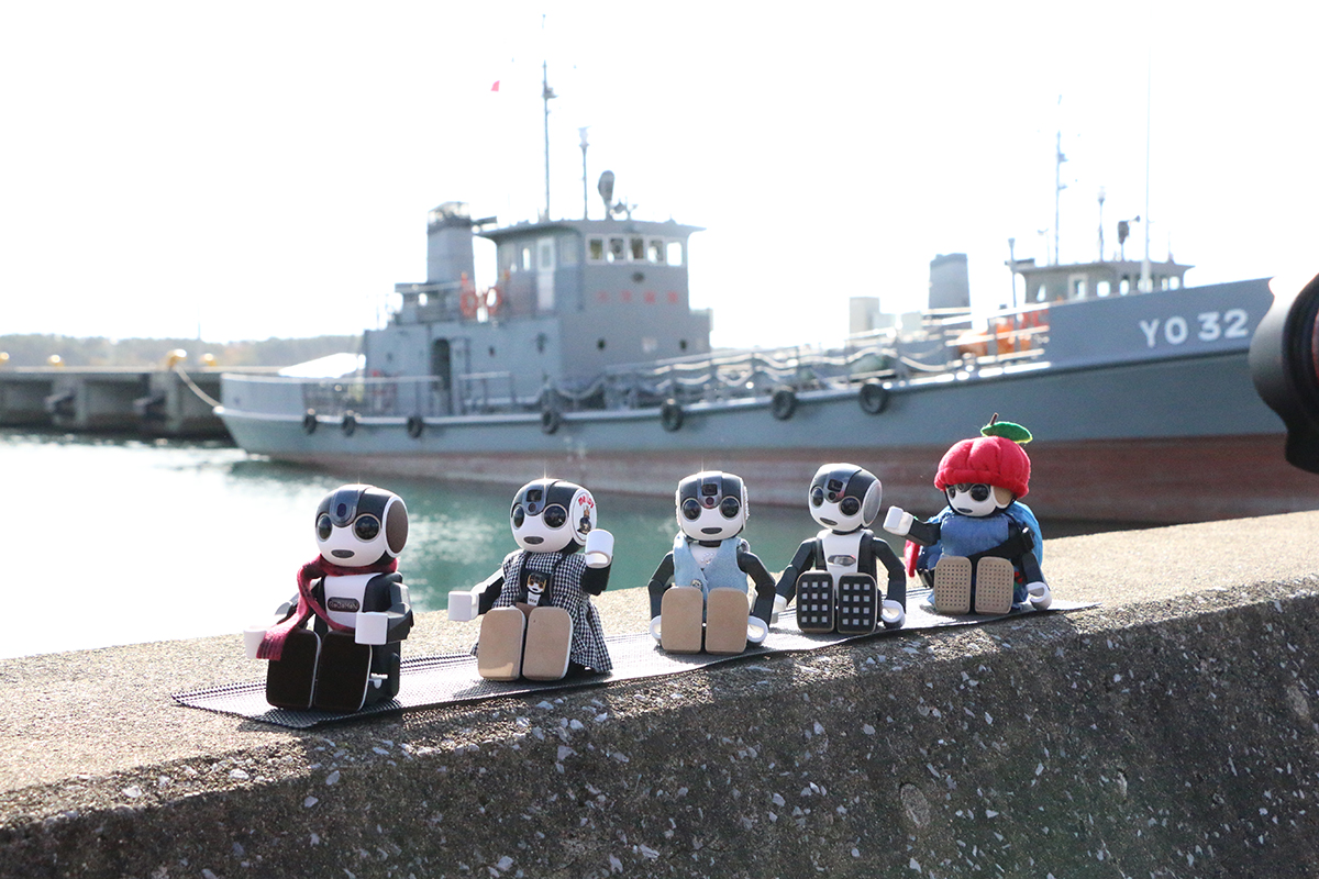 RoBoHoN robots arrayed with the Ominato base of the Maritime Self-Defense Force in the background. | MUTSU CITY