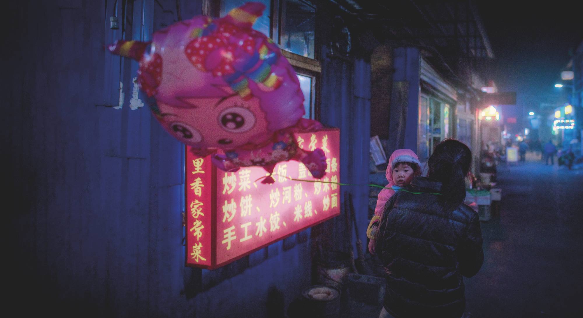 A woman carries a young girl in the migrant village of Heiqiaocun in Beijing in February 2017. | NICOLAS ASFOURI / AFP / via Getty Images
