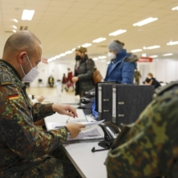 German Army soldiers assist the administration of COVID-19 vaccinations at a vaccine center in Munich, Germany, on Thursday. Germany is poised to clamp down on people who are not vaccinated against COVID-19 and drastically curtail social contacts, to ease pressure on increasingly stretched hospitals. | BLOOMBERG