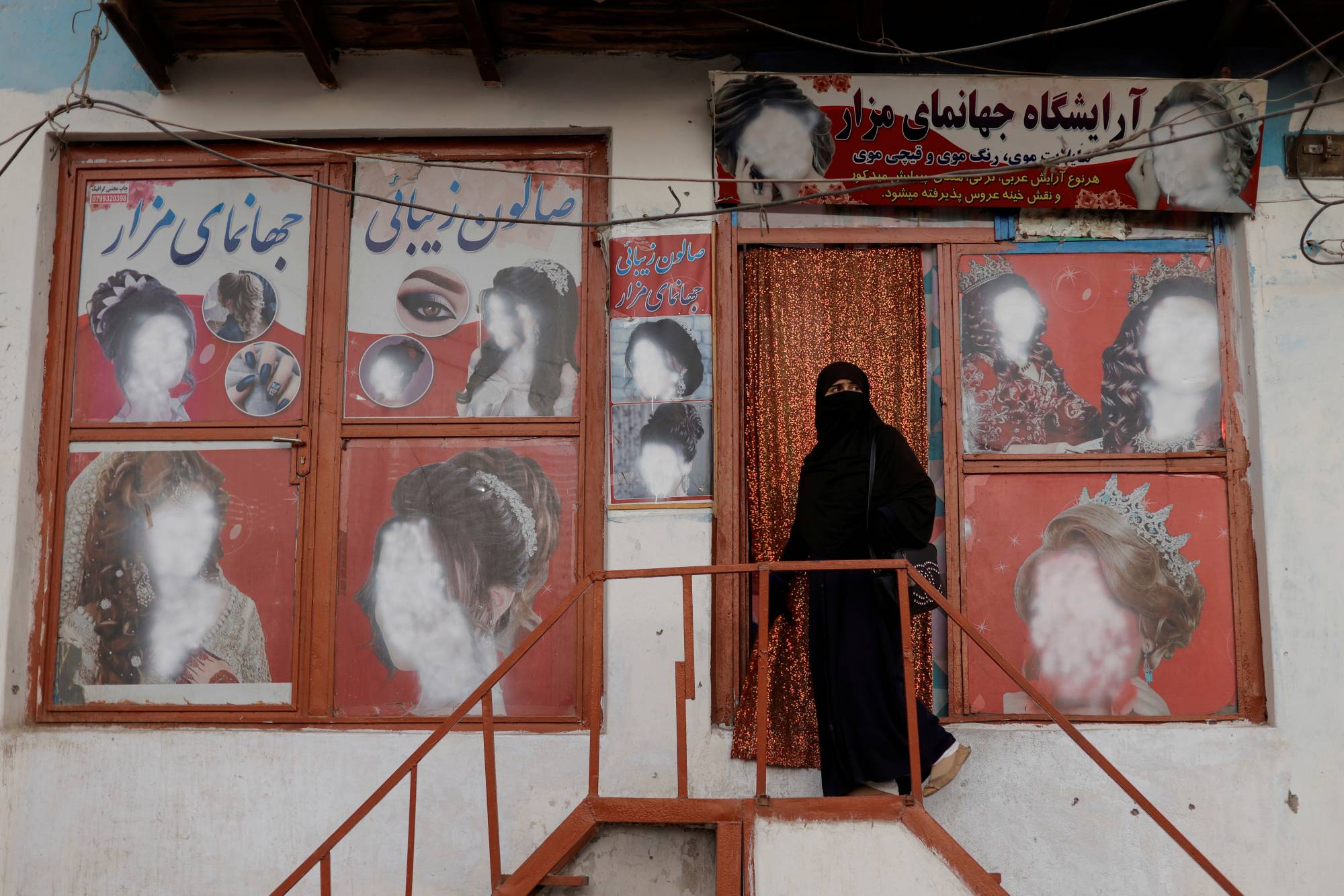 A woman wearing a niqab enters a beauty salon in Kabul where ads depicting women have been defaced by a shopkeeper. | REUTERS