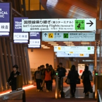 Quarantine support members walk on at the international flight arrival floor at Tokyo\'s Haneda Airport on Wednesday. | AFP-JIJI