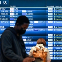 People stand in front of an arrivals board showing cancelled flights at Tokyo\'s Haneda Airport on Tuesday. | AFP-JIJI