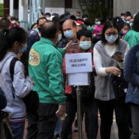 People wearing face masks line up outside a community vaccination center to receive a dose of Sinovac Biotech\'s CoronaVac COVID-19 vaccine in Hong Kong on Thursday. | REUTERS
