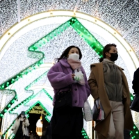 People wearing masks walk under a Christmas illumination at a shopping district in central Seoul on Dec. 1. | REUTERS
