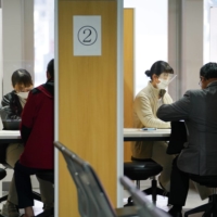 Workers wearing protective masks talk to travelers at a COVID-19 testing center at Narita Airport on Nov. 30. | BLOOMBERG