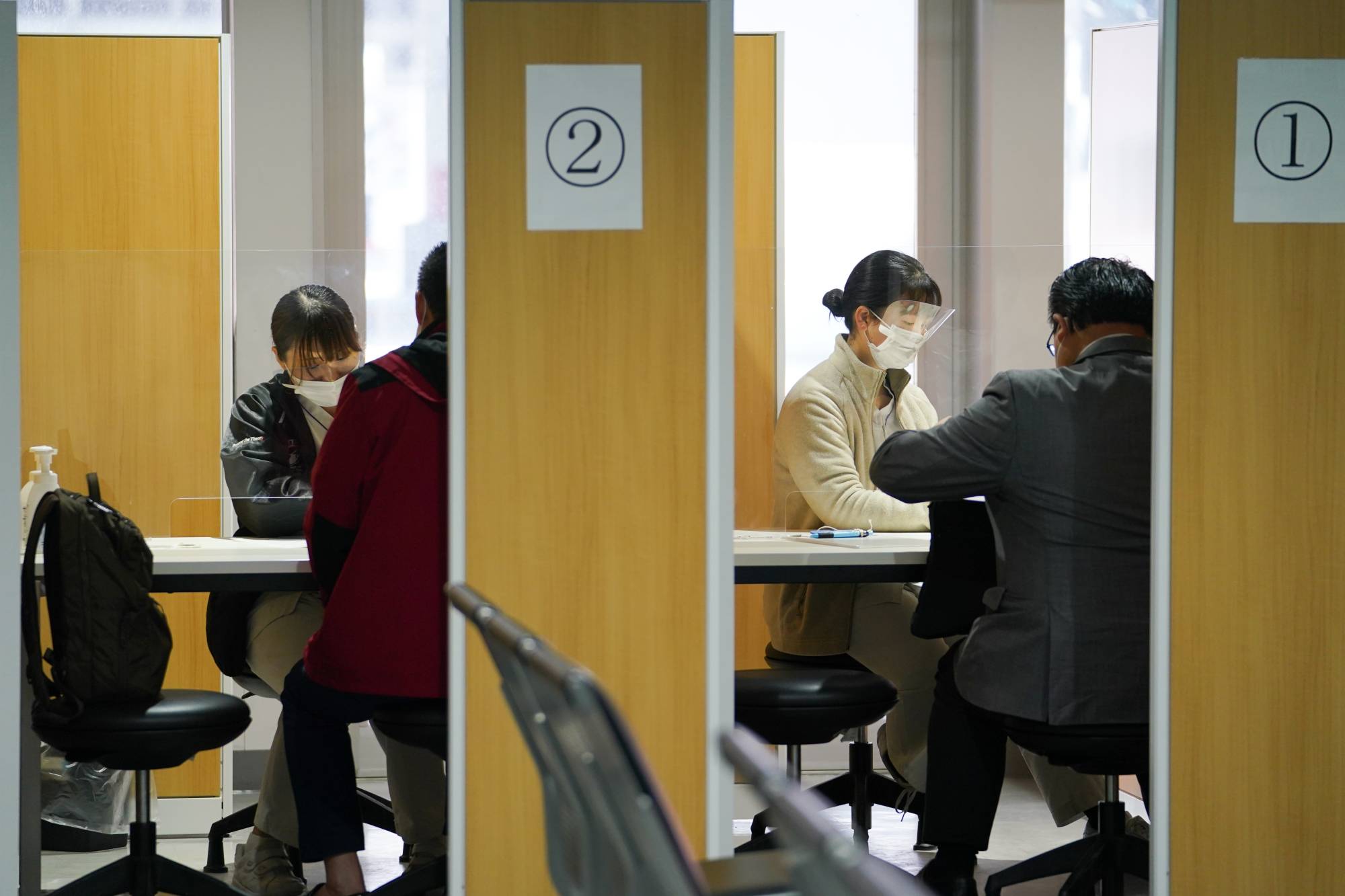 Workers wearing protective masks talk to travelers at a COVID-19 testing center at Narita Airport on Nov. 30. | Bloomberg