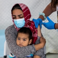 A migrant holds her baby as she receives a shot of the Johnson & Johnson COVID-19 vaccine in the Mavrovouni camp for refugees and migrants on the island of Lesbos, Greece, June 3, 2021.  | REUTERS