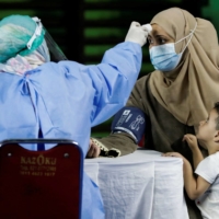 A woman undergoes a health screening before receiving a dose of a COVID-19 vaccine during a mass vaccination program for asylum seekers and refugees at a sports hall in Jakarta in Oct., 2021. | REUTERS