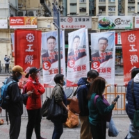 People queue up for a free bus service in front of campaign flags on the Legislative Council Election Day, during which Hong Kong offered free travel on most forms of public transport. | REUTERS