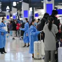 Employees in personal protective equipment (PPE) assist travelers at a China Eastern Airlines check-in counter at Narita Airport in Chiba Prefecture on Nov. 30. | BLOOMBERG