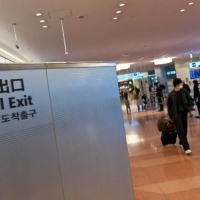 A traveler walks past an exit on the international arrivals floor of Tokyo\'s Haneda Airport on Dec.1. | AFP-JIJI