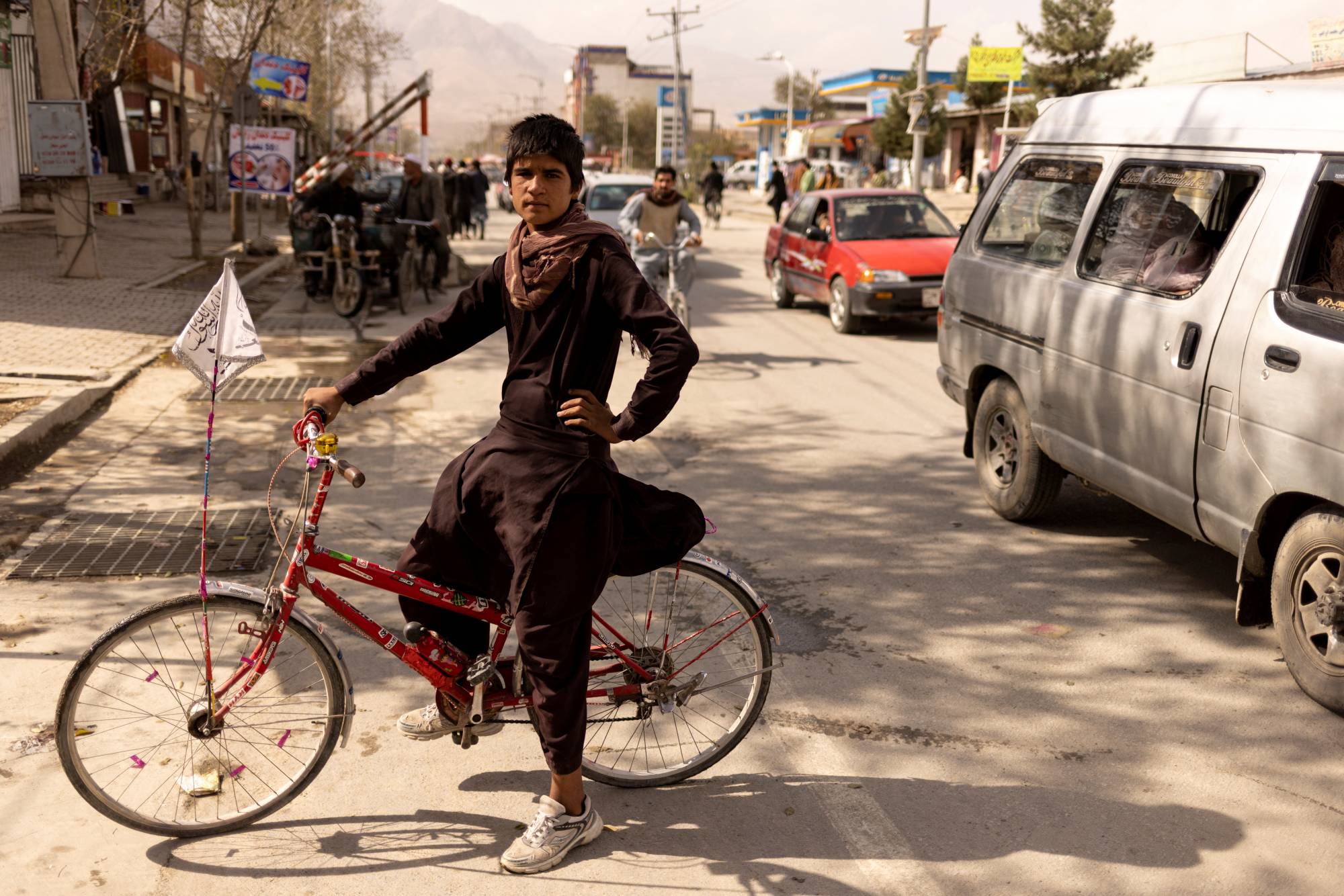 Wafiullah, 15, sits on his bike, which has an Islamic Emirate flag hanging on it, in front of a Taliban checkpoint in Kabul. | Reuters
