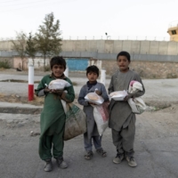 Children carry bags of food in front of the concrete wall of a former U.S. Army base in Kabul on Oct. 16.  | REUTERS