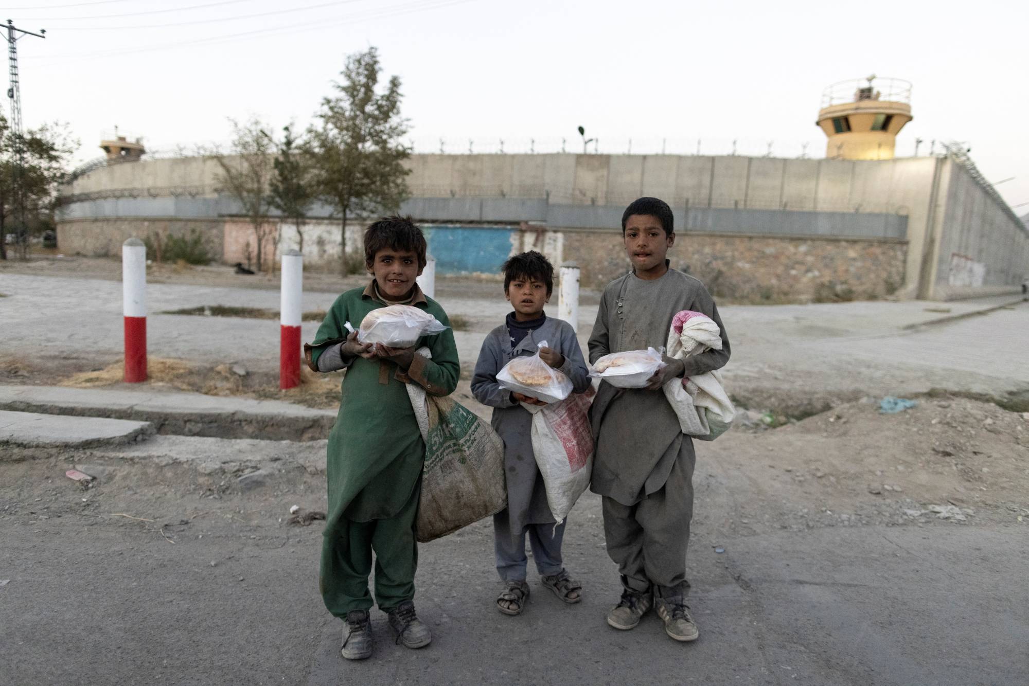 Children carry bags of food in front of the concrete wall of a former U.S. Army base in Kabul on Oct. 16. | Reuters