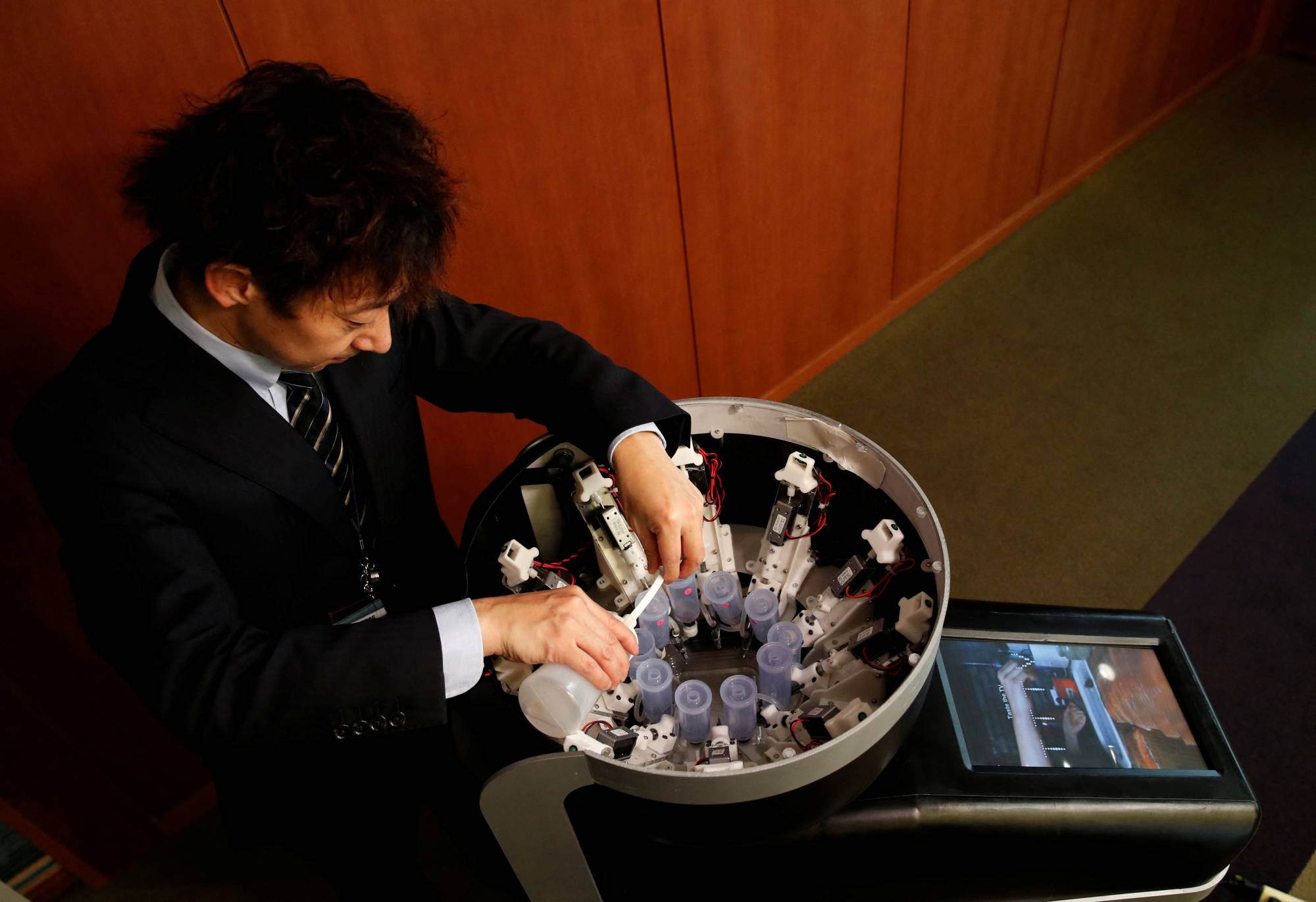 Meiji University professor Homei Miyashita fills flavor canisters as he demonstrates Taste the TV (TTTV), a prototype lickable TV screen that can imitate the flavors of various foods, at the university in Tokyo on Wednesday. | Reuters