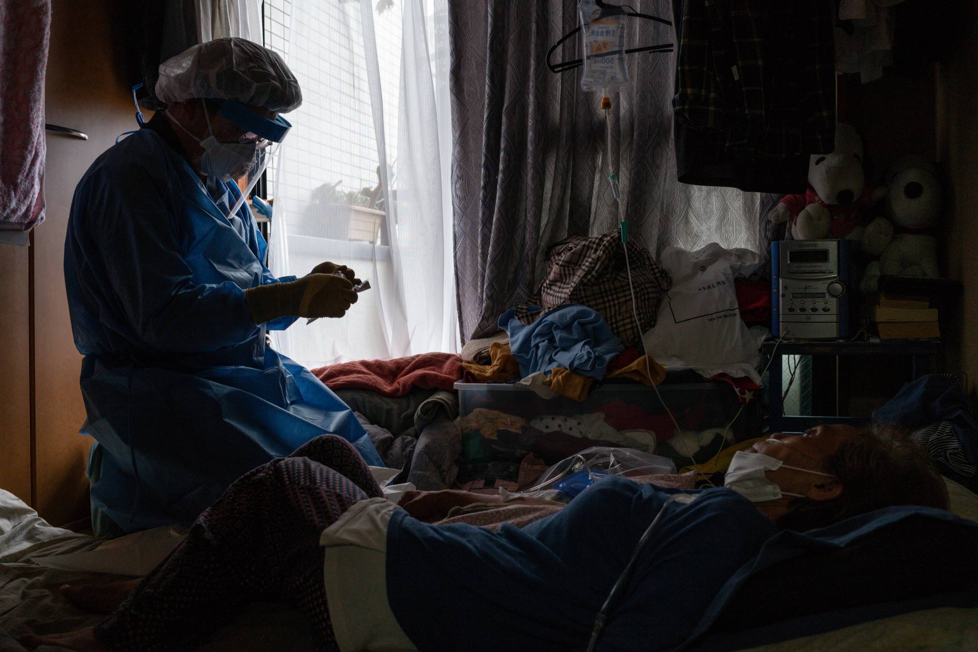 Ryoichi Ichihashi, founding director of the General Home Care Clinic in Gifu Prefecture, checks on a bedridden mother infected with COVID-19 in Tokyo in early September. | RYUSEI TAKAHASHI 