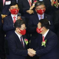 Yoon Suk-yeol (front right), the presidential election candidate for South Korea\'s main opposition People Power Party, shakes hands with Lee Jae-myung (front left), the candidate for the ruling Democratic Party, after a ceremony to mark the first stock trading day of the year at the Korea Exchange in Seoul on Monday. | AFP-JIJI