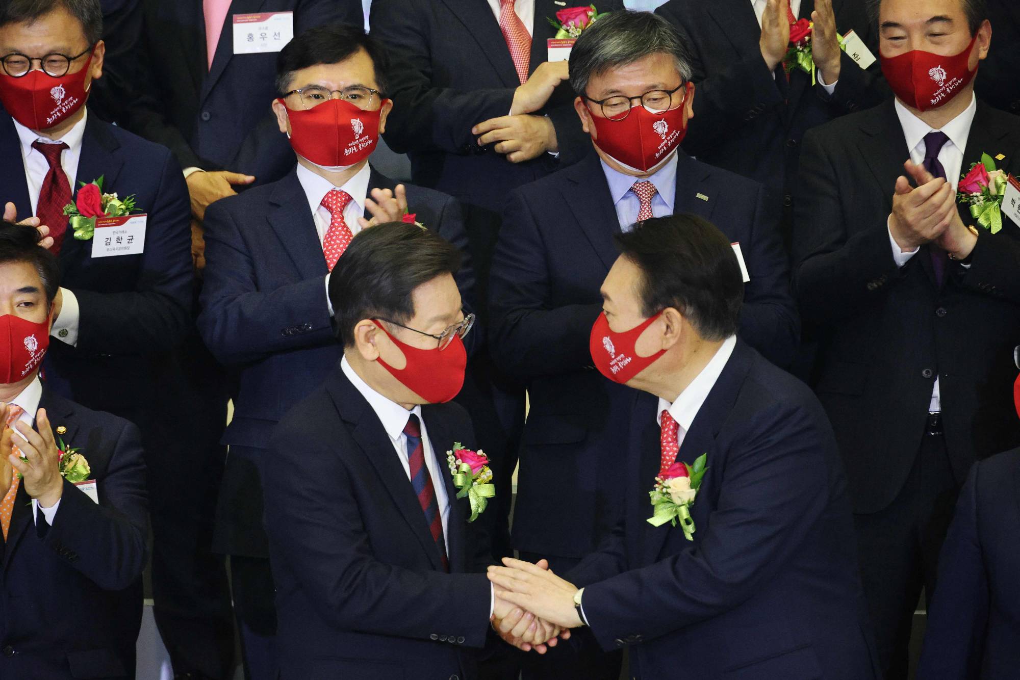 Yoon Suk-yeol (front right), the presidential election candidate for South Korea's main opposition People Power Party, shakes hands with Lee Jae-myung (front left), the candidate for the ruling Democratic Party, after a ceremony to mark the first stock trading day of the year at the Korea Exchange in Seoul on Monday. | AFP-JIJI