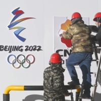 Workers put up the Beijing Olympics logo in Beijing in December. | KYODO
