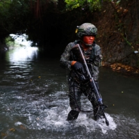 An ARP trainee dressed in camouflage wades through sewage contaminated water.  | REUTERS