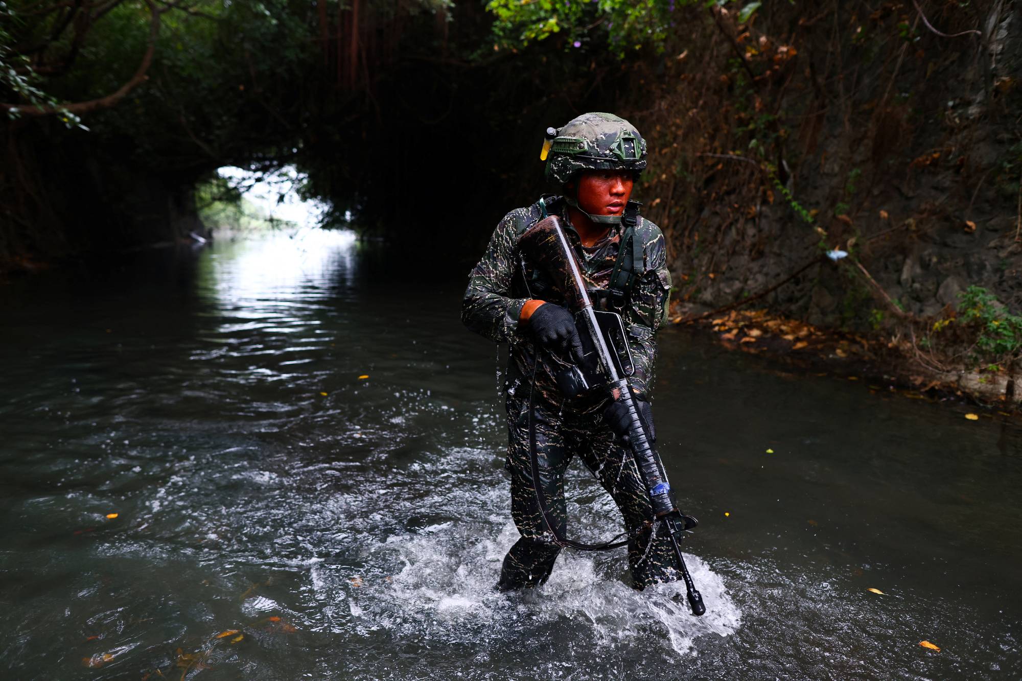 An ARP trainee dressed in camouflage wades through sewage contaminated water. | Reuters