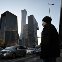A man waits to cross a road in the central business district in Beijing. China\'s strong recovery from the COVID-19 pandemic is threatened by omicron and a property sector slowdown.  | AFP-JIJI