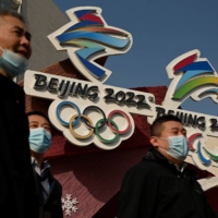 People walk past the logos of the 2022 Winter Olympics and Paralympics in Beijing on Tuesday. | AFP-JIJI