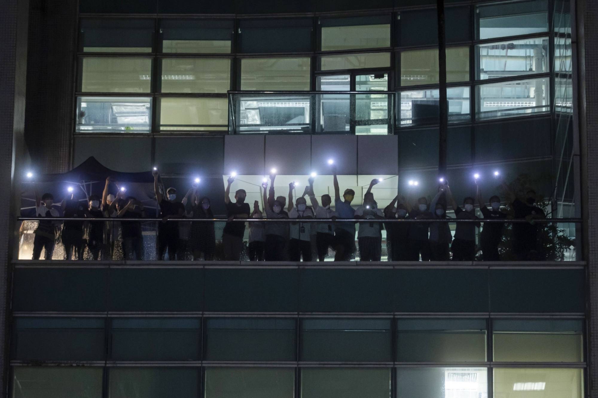 Workers illuminate mobile phone torches from a balcony at the headquarters of the Apple Daily newspaper and its publisher Next Digital Ltd. in Hong Kong, China, on Wednesday, June 23, 2021. | Bloomberg