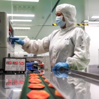 A worker produces face masks for athletes, staff members and volunteers of the Beijing 2022 Winter Olympic Games at a factory in Binzhou in China\'s eastern Shandong province on Thursday. | AFP-JIJI