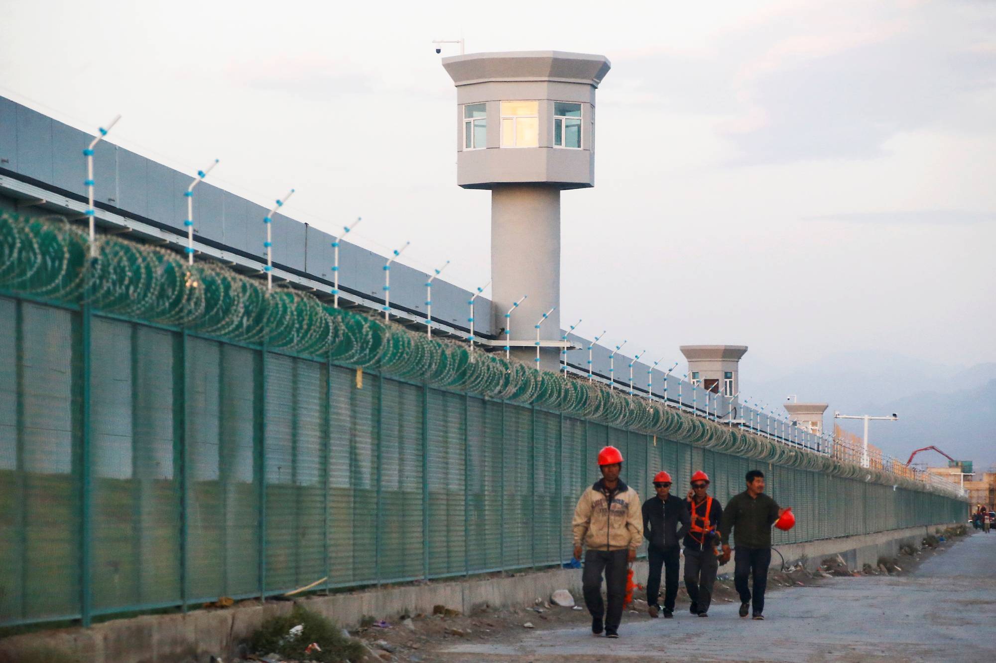 Chinese workers walk by the perimeter fence of what could be the world's largest detention facility, officially called a 'vocational skills education center,' located in Dabancheng, Xinjiang Uyghur Autonomous Region, China, in September 2018.   | REUTERS 