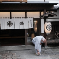A person dressed in a yukata robe puts on sandals in front of a hotel at the Kusatsu hot springs resort in Kusatsu, Gunma Prefecture. | BLOOMBERG
