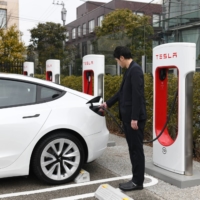 Tetsuya Arai connects a charging plug to his Tesla at the Daikanyama EV Supercharger station in Tokyo. | BLOOMBERG