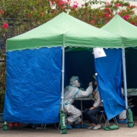 A health worker collects a swab sample at a COVID-19 testing facility in Hong Kong on Wednesday. Hong Kong took the unprecedented step of forcing residents of a sprawling neighborhood to test for COVID-19 as authorities try to control an outbreak of the omicron variant that has seen cases doubling every few days. | BLOOMBERG