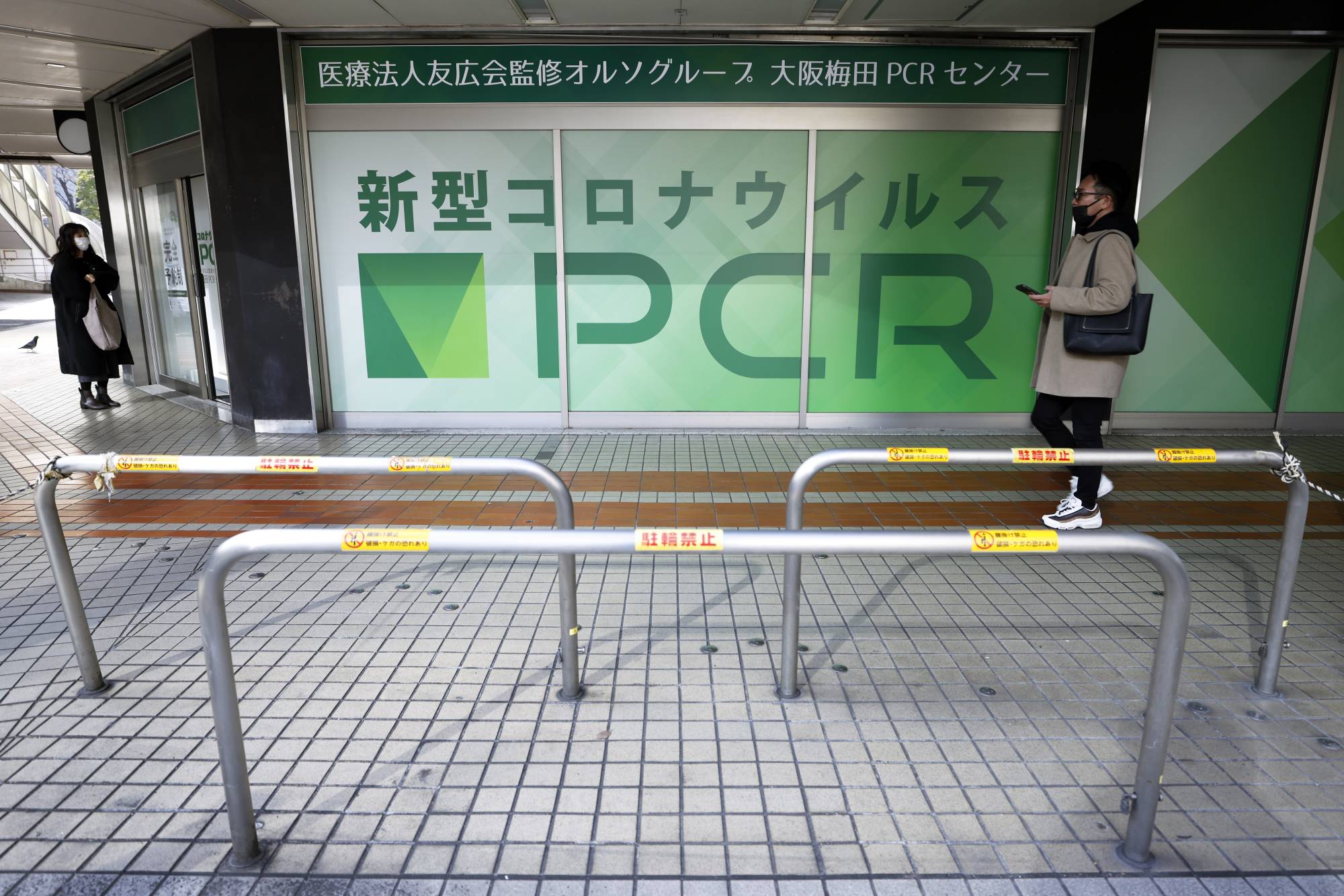A person waits outside a PCR testing site in Osaka on Jan. 27. Although Japan is apparently past the peak of the omicron-driven sixth wave, shortages of antigen and PCR tests are still commonplace. | BLOOMBERG