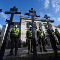 Ukrainian security forces stand guard after activists set up symbolic tomb crosses with the inscription \"Russian occupiers\" during a rally outside the Russian Embassy in Kyiv on Tuesday.   | AFP-JIJI