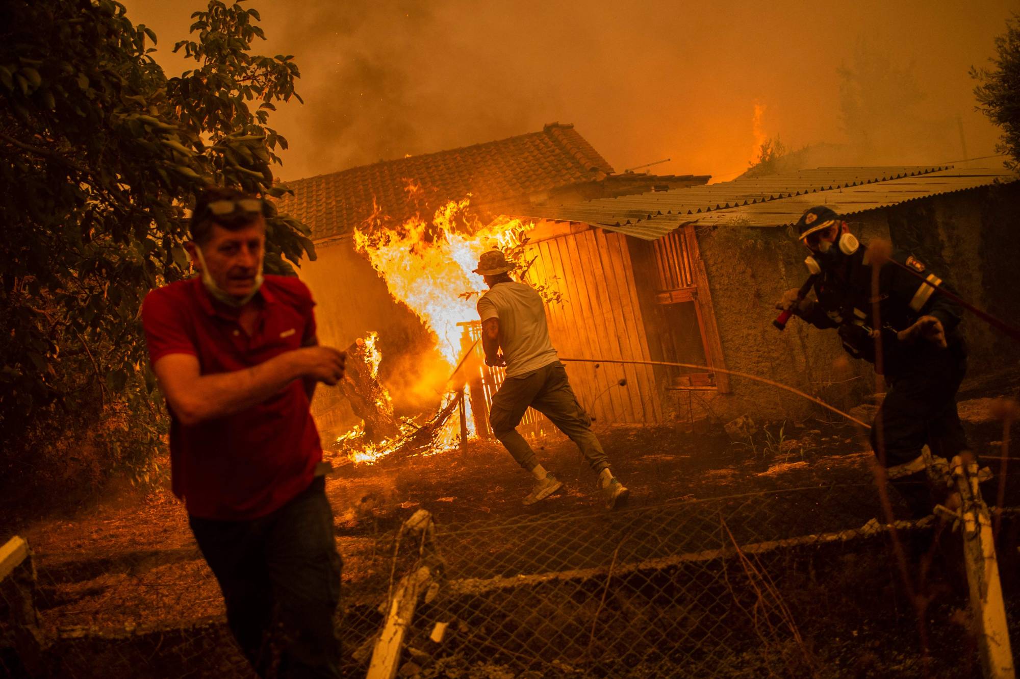 A firefighter and local residents rush to a burning house in an attempt to extinguish forest fires that are approaching the village of Pefki on Evia island, Greece, in August 2021 | AFP-JIJI