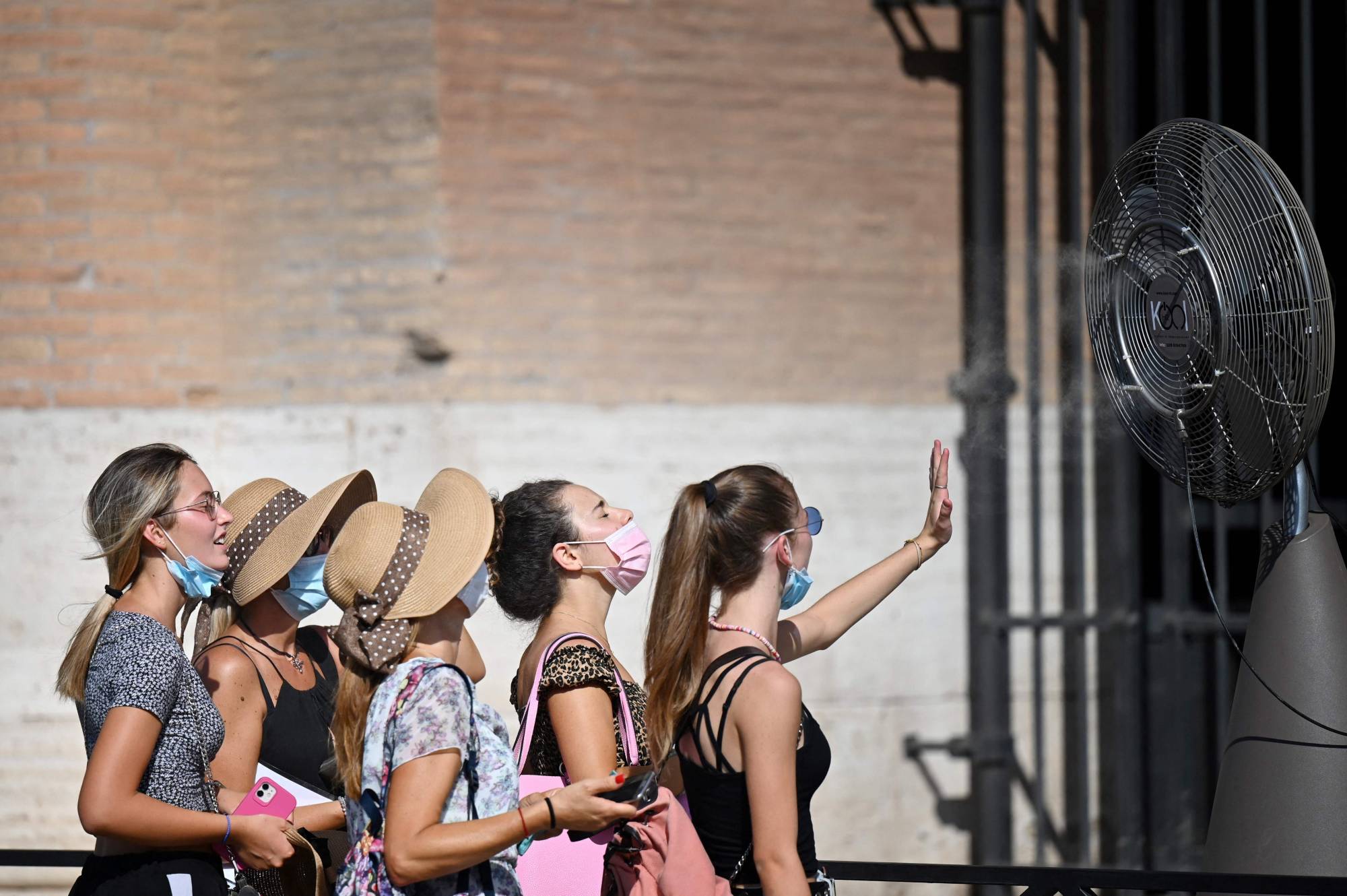 A group of women cool off in front of a fan during a heat wave in August 2021 as they queue at the entrance of The Colosseum in Rome. | AFP-JIJI