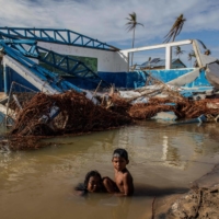 Children bathe next to a destroyed house in Haulover, Nicaragua, in November 2020 days after the passage of Hurricane Iota. | AFP-JIJI
