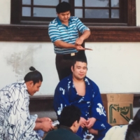 A rikishi having his topknot fixed while another plays a Gameboy. | KATRINA WATTS
