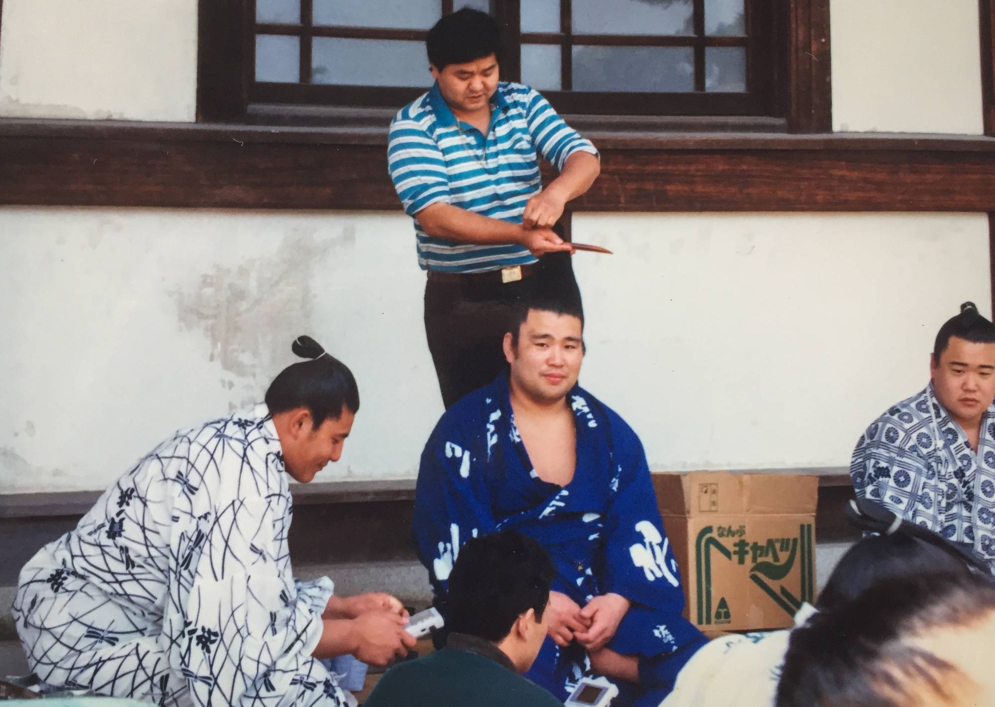 A rikishi having his topknot fixed while another plays a Gameboy. | Katrina Watts 