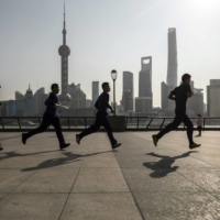 Joggers run along the Bund in front of buildings in the Lujiazui Financial District across the Huangpu River in Shanghai on Feb. 27. China\'s Politburo vowed to strengthen macroeconomic policies to stabilize the economy this year, suggesting more support could be on the cards to boost growth ahead of a key leadership meeting later this year. | BLOOMBERG
