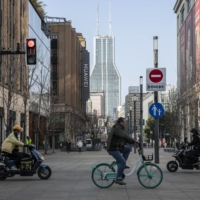 Cyclists and motorcyclists rides along Nanjing road in Shanghai on Feb. 27. China\'s Politburo vowed to strengthen macroeconomic policies to stabilize the economy this year, suggesting more support could be on the cards to boost growth ahead of a key leadership meeting later this year. | BLOOMBERG