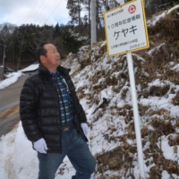 Toshio Hirono looks at a sign noting a commemorative tree planting by Yamakiya Elementary School’s forestry club at the entrance of Daini Oyako no Mori forest in Kawamata, Fukushima Prefecture. | FUKUSHIMA MINPO
