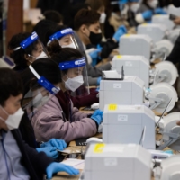 Workers check voters information at an early polling location for the presidential election in Seoul on Friday. South Korea kicked off two days of early voting Friday as the country battles a record wave of coronavirus infections, while data showed inflation unexpectedly accelerated in February as rising costs weighed on voters. | BLOOMBERG