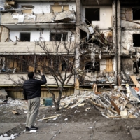 Ukrainians survey debris after a residential building was hit by missiles in the country’s capital of Kyiv on Feb. 25. As Ukrainians deal with the devastation of the Russian attacks in their homeland, many are also encountering a confounding and almost surreal backlash from family members in Russia, who refuse to believe that Russian soldiers could bomb innocent people, or even that a war is taking place at all. | LYNSEY ADDARIO / THE NEW YORK TIMES
